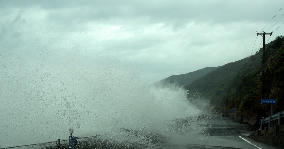 Storm waves breaking over a seawall and flooding a coastal road in Japan during a typhoon