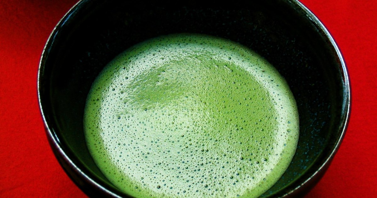 A black tea bowl holding whisked green matcha covered in a fine layer of pale foam