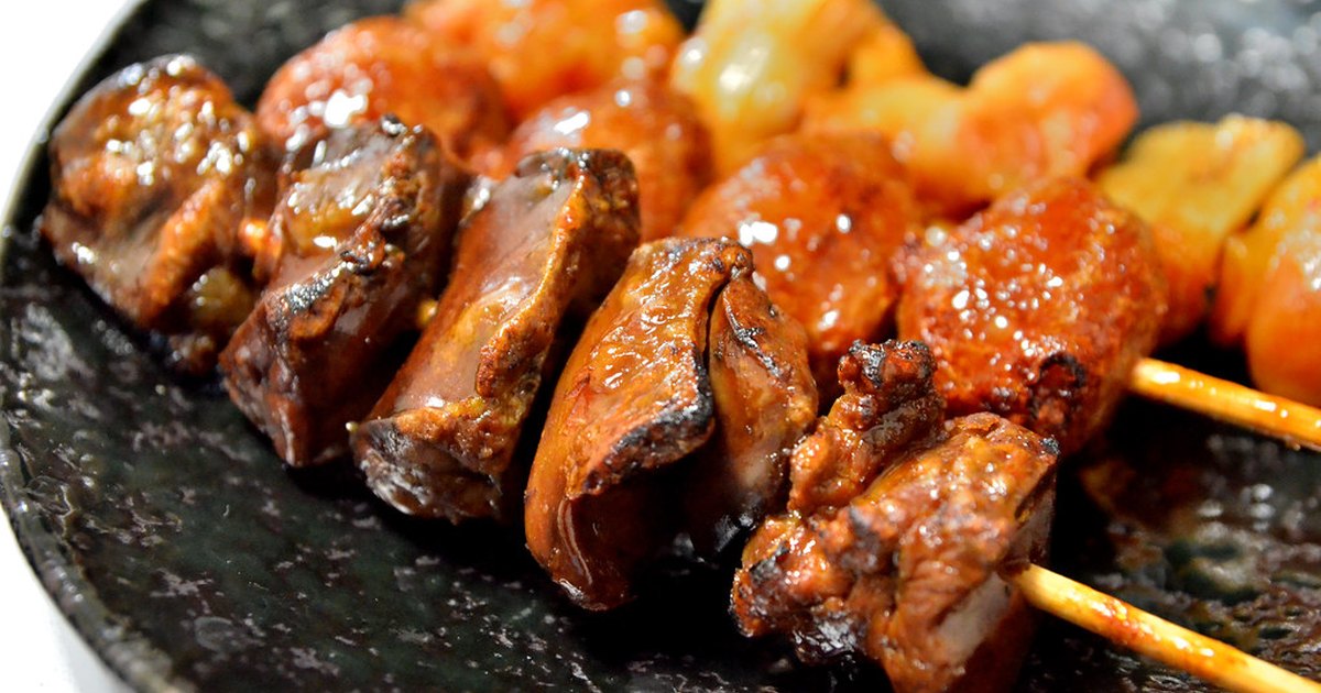 Grilled chicken skewers glazed dark brown with tare sauce on a black ceramic plate