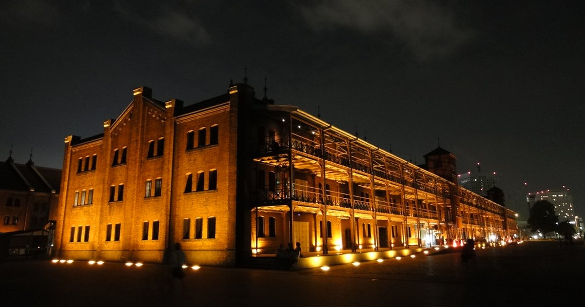 The Yokohama Red Brick Warehouse lit up at night, with the harbor promenade in front and Minato Mirai towers behind