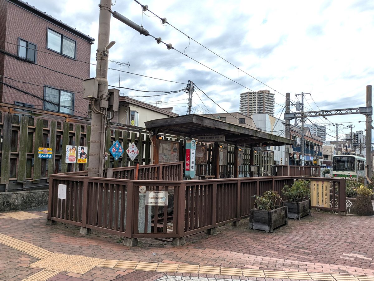 Minowabashi tram stop with a wooden fence and a green and white tram in the distance