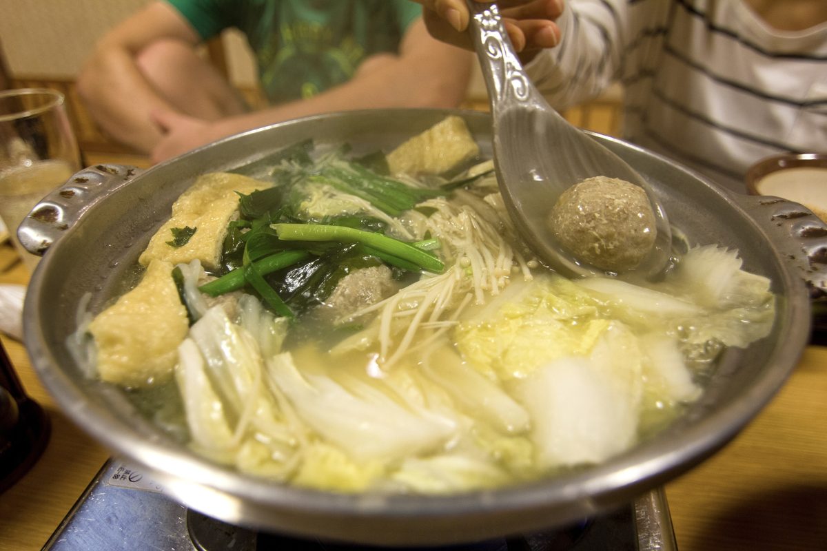 A pot of chanko nabe with chicken meatballs, fried tofu, cabbage and enoki mushrooms