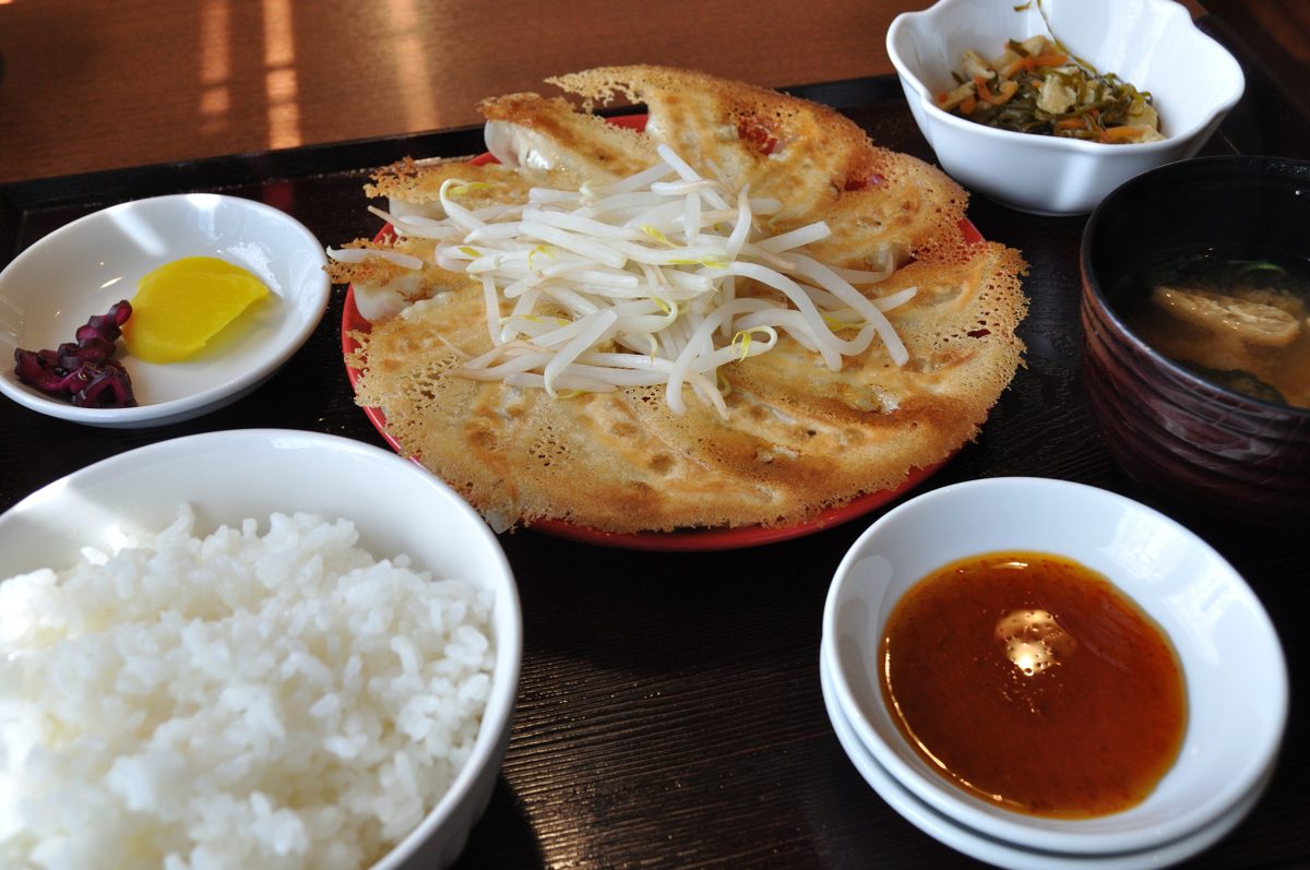 A gyoza set meal with a circle of pan-fried gyoza topped with bean sprouts, rice, pickles and dipping sauce