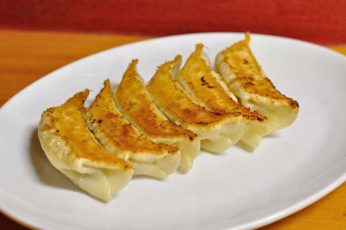 Six pan-fried gyoza with crisp golden bottoms on a white plate