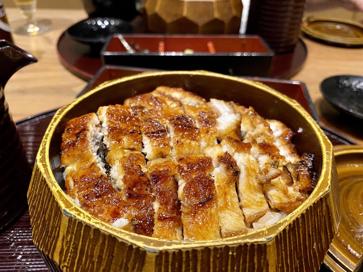 Strips of grilled eel on rice in a lacquered hitsumabushi tub, with side dishes behind
