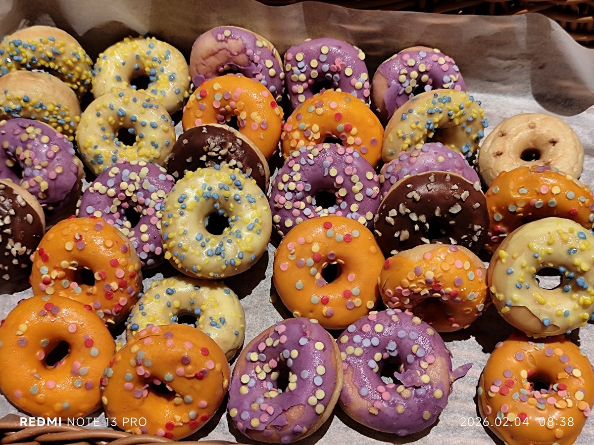 A tray of colorful iced doughnuts with sprinkles at a hotel breakfast buffet
