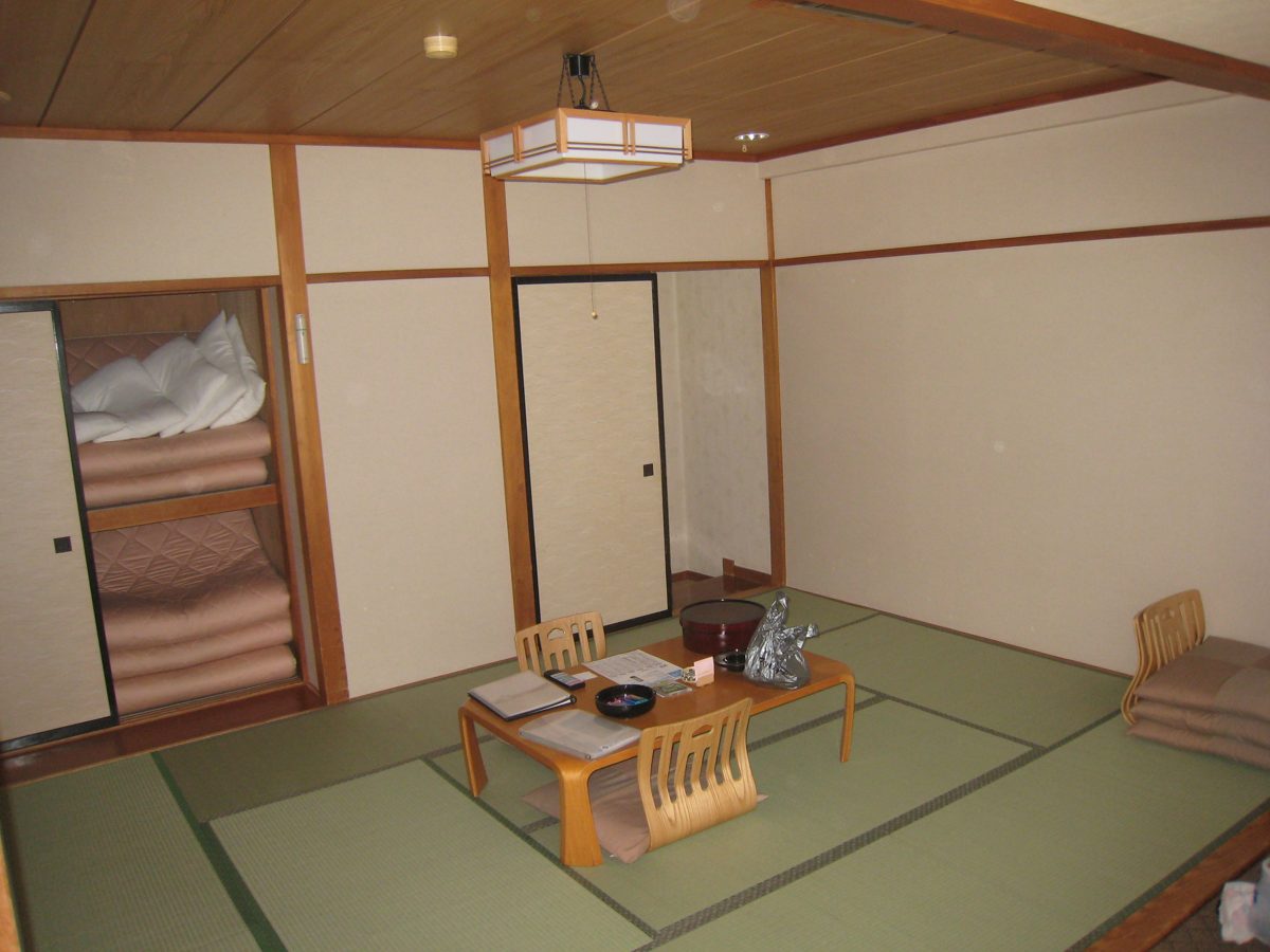 A Japanese-style tatami room with a low table and futon bedding stacked in an open closet