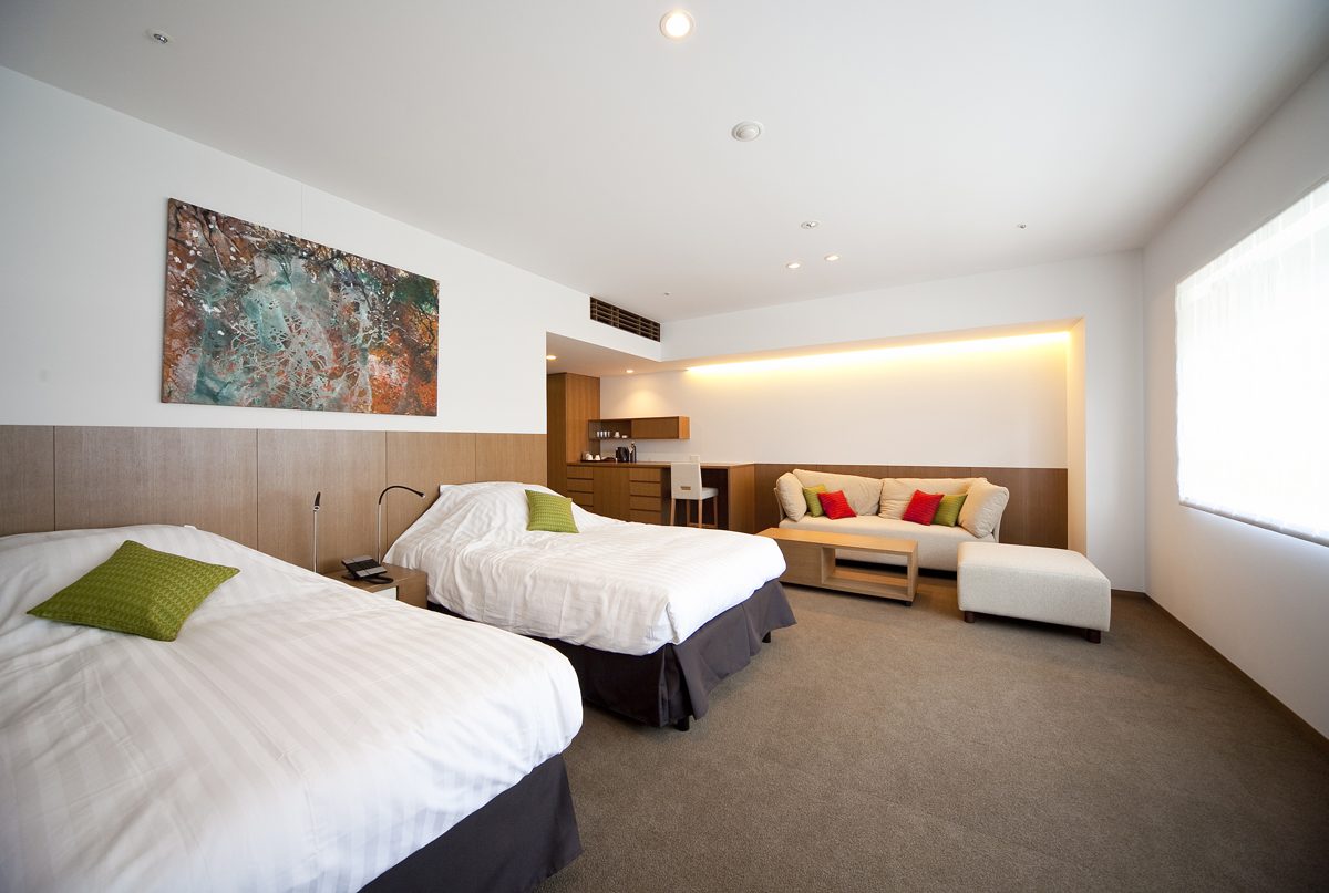 A large western-style twin room with two beds, a sofa and a long window