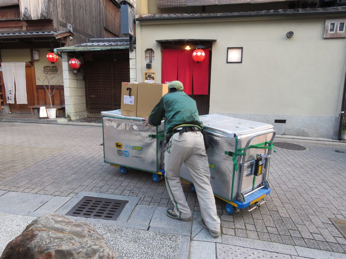 A delivery worker pushing a metal parcel cart on a stone-paved street