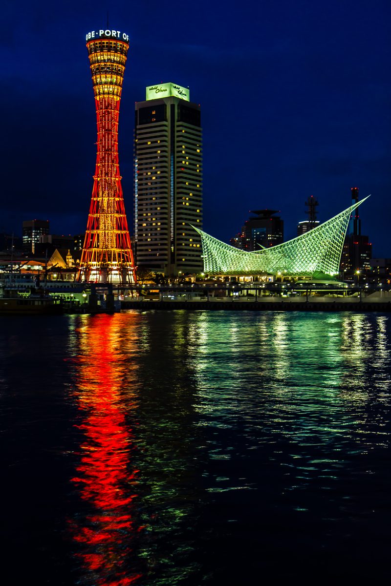 Kobe Port Tower and the Kobe Maritime Museum lit up at night, reflected in the harbor
