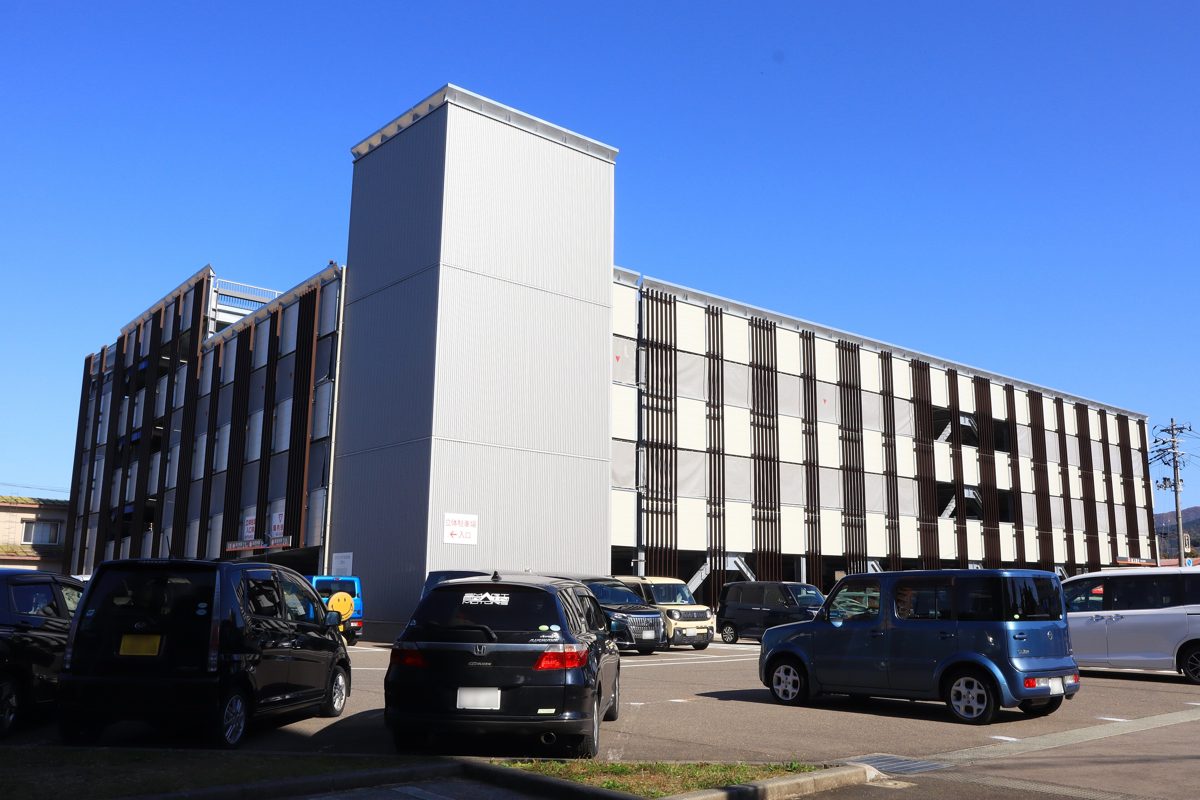 A multi-storey municipal car park with cars parked in front, under a blue sky