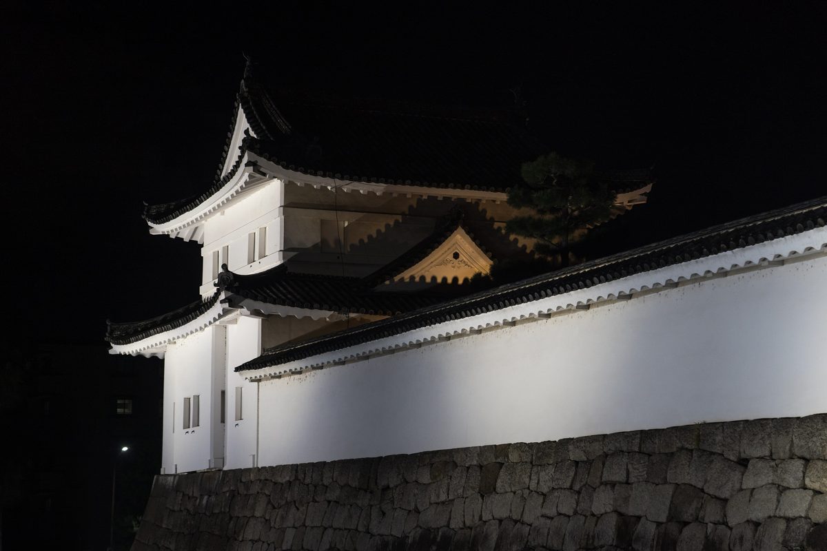The southeast corner watchtower of Nijo Castle lit up at night above its stone wall