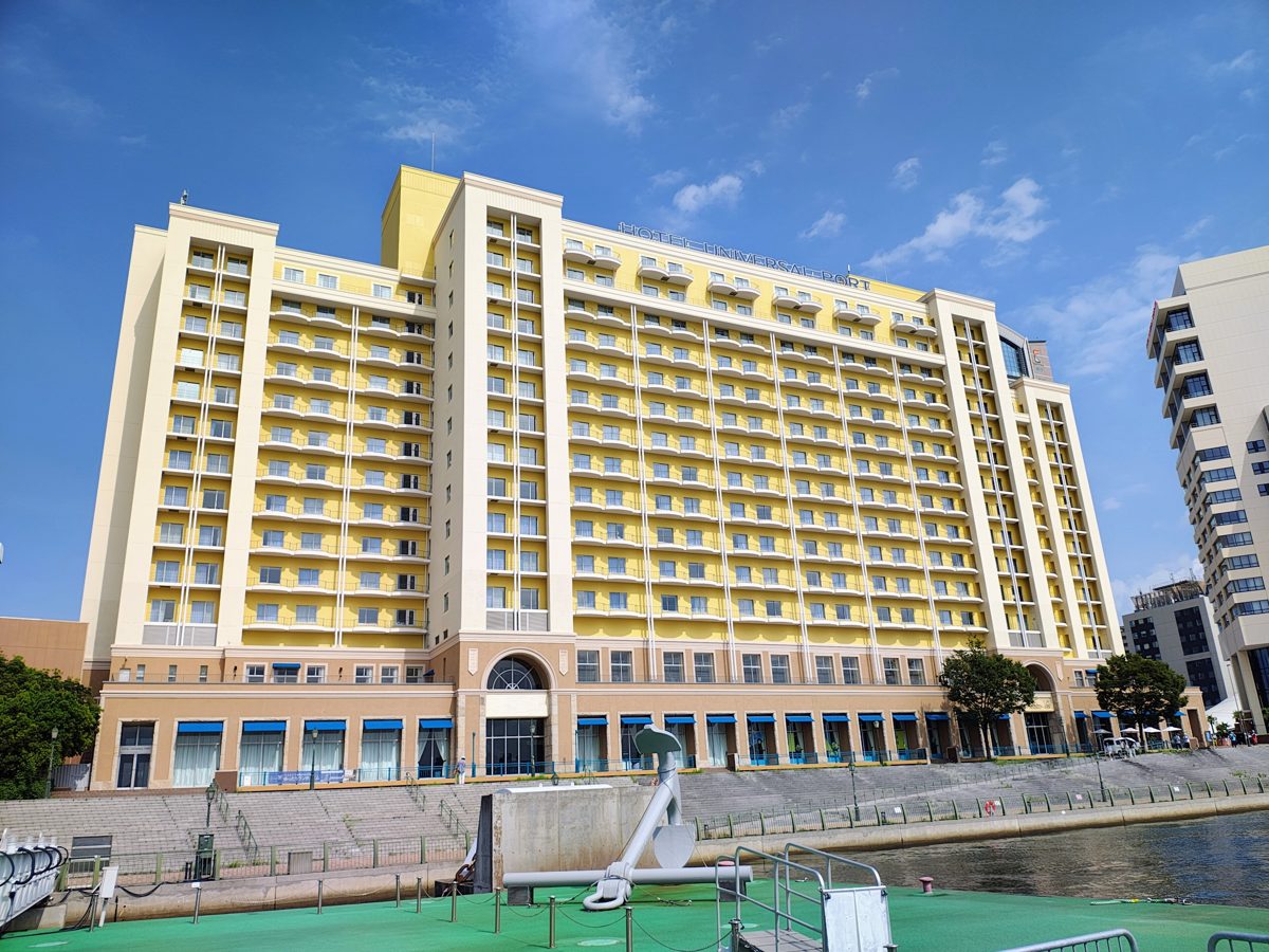 The yellow and cream tower of Hotel Universal Port, seen from the water under a blue sky