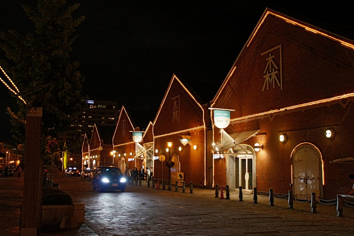 Red brick warehouses lit up at night along a cobbled street