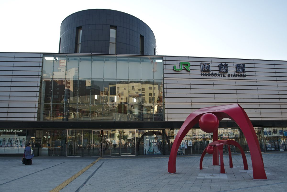 The front of JR Hakodate Station with a red sculpture in the plaza