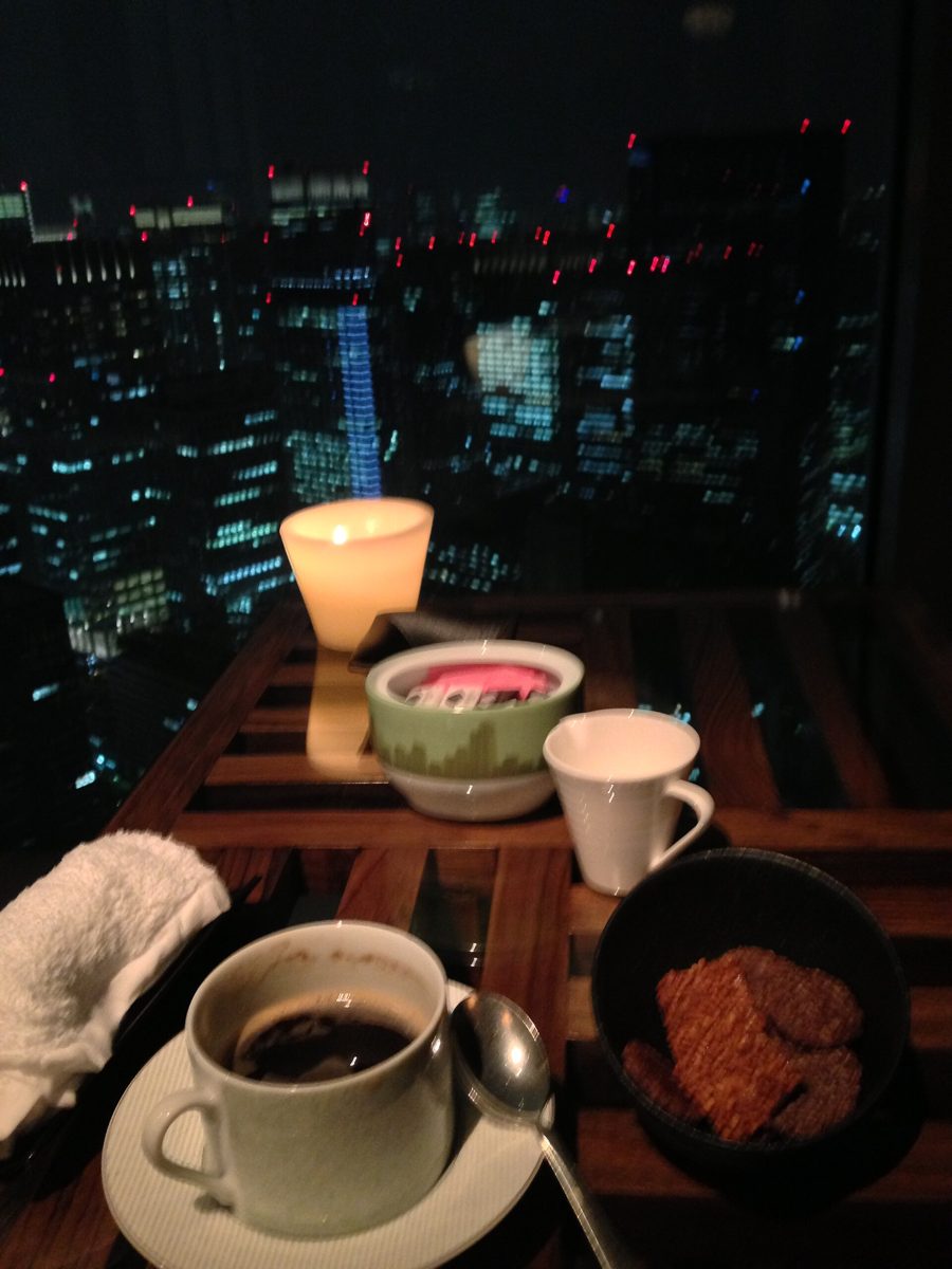 Coffee, cookies and a small dessert on a wooden table by a window over the city at night