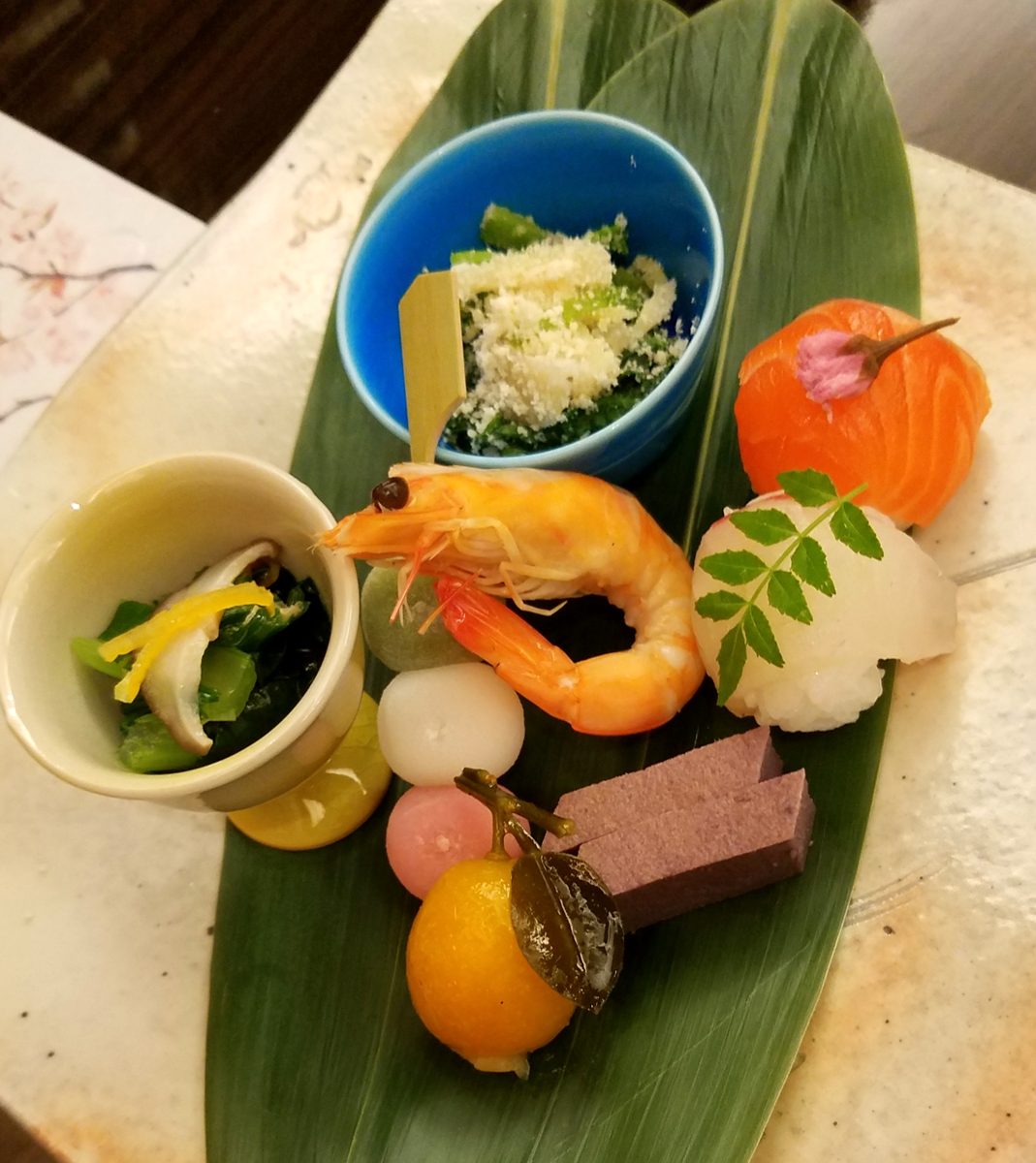 A starter plate of small dishes, including a prawn and sushi, on a bamboo leaf
