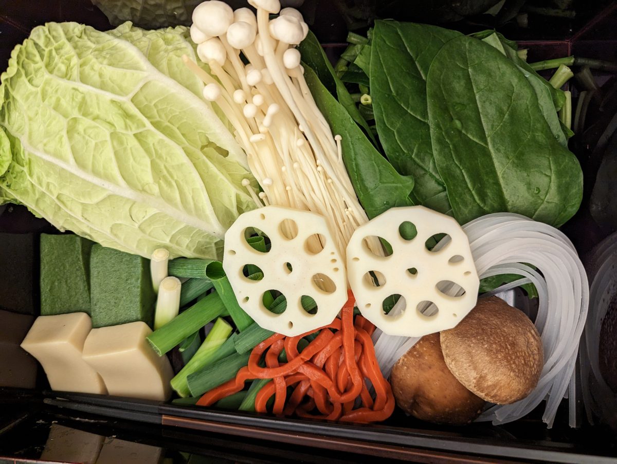 A plate of vegetables, mushrooms, tofu and noodles for a shabu-shabu course