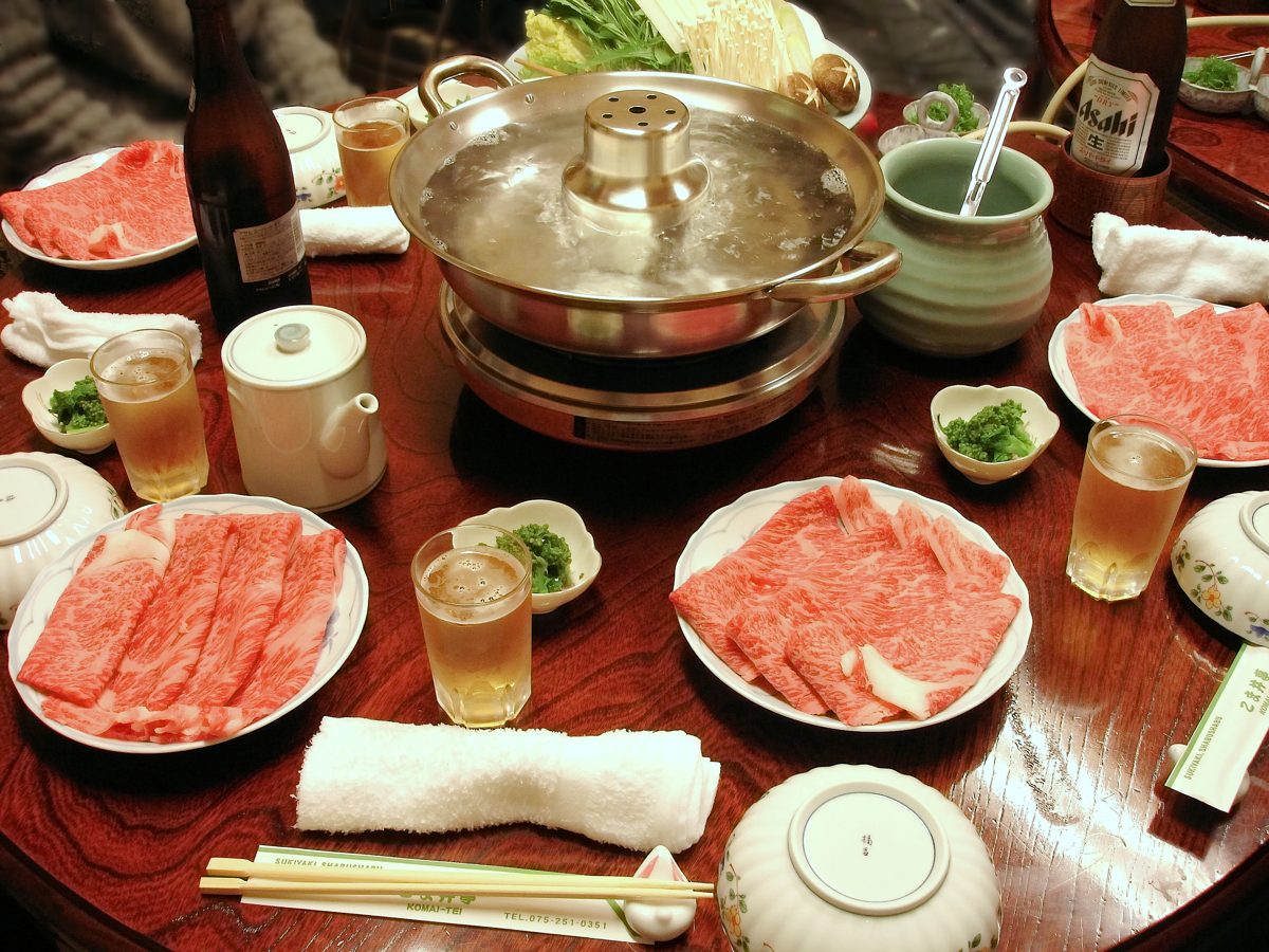 A shabu-shabu table with a hot pot and plates of thinly sliced marbled beef