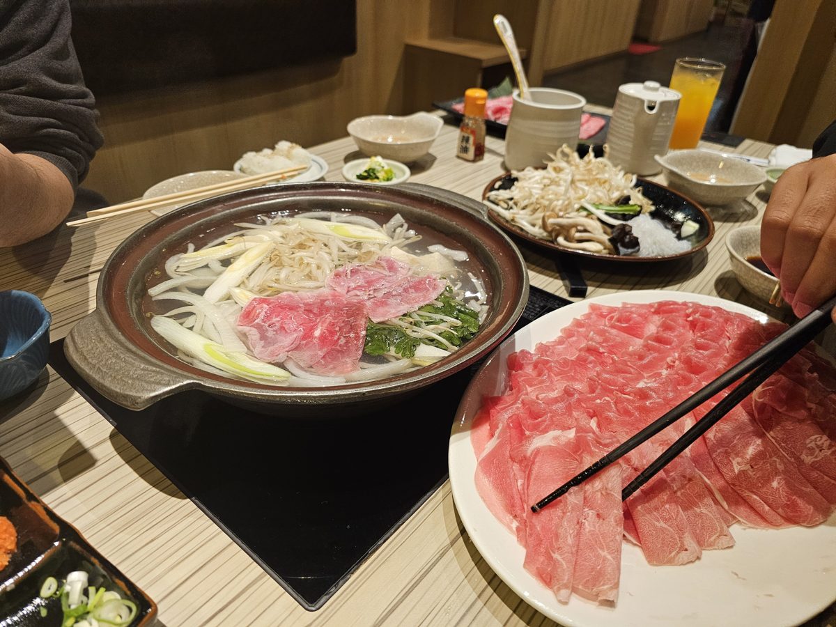 A clay hot pot with pork and vegetables beside a plate of sliced meat
