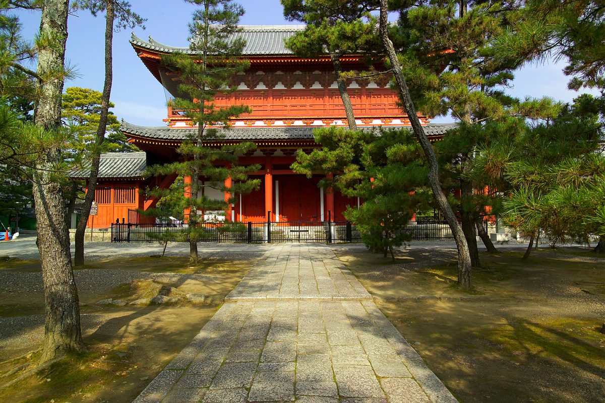 The red two-story Sanmon gate of Myoshinji behind pine trees and a stone path