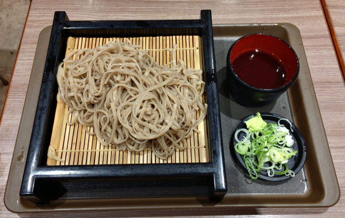 Mori soba on a bamboo mat with dipping sauce and sliced green onion on a tray
