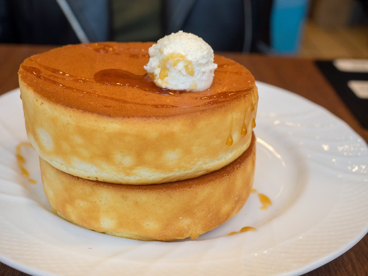 Two thick, fluffy Japanese pancakes on a white plate, topped with whipped butter