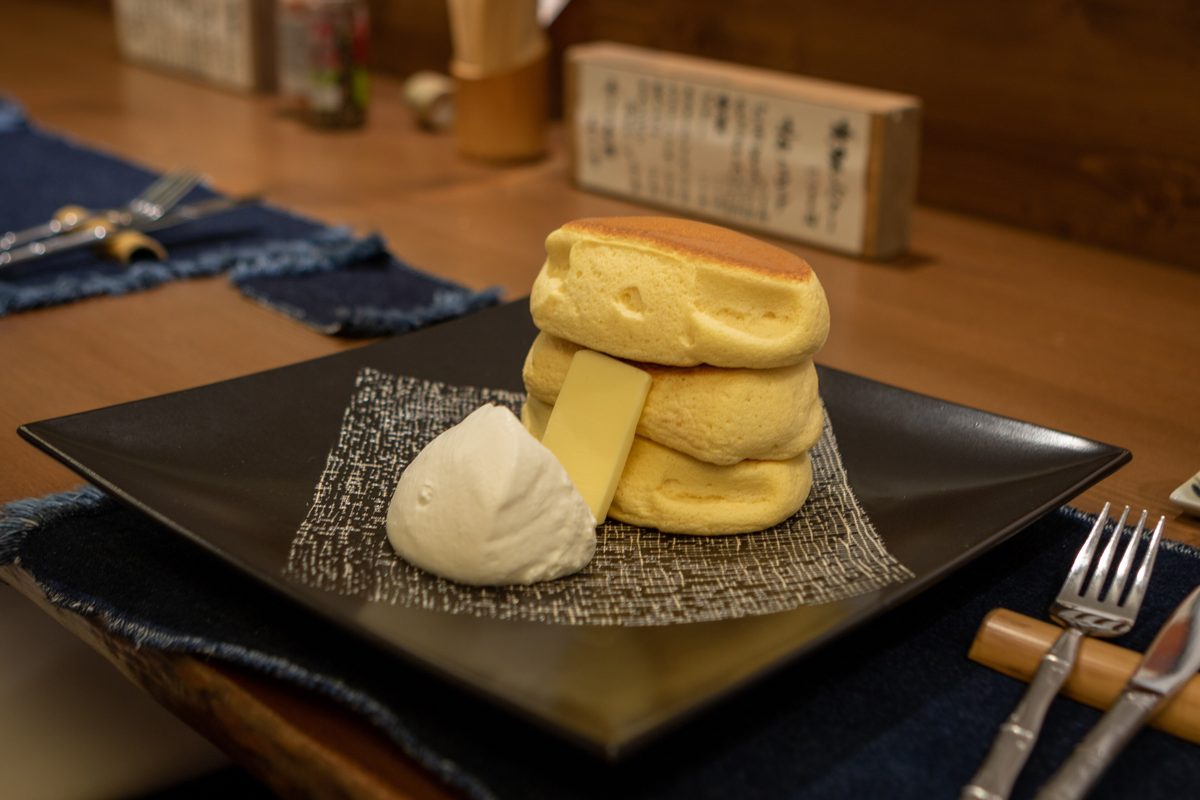 A stack of fluffy pancakes with butter and cream on a dark square plate