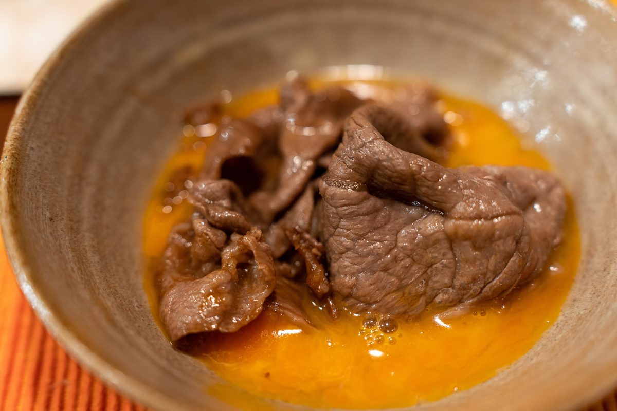Cooked beef resting in a bowl of beaten raw egg