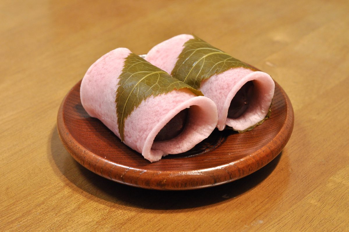Two pink sakura-mochi wrapped in cherry leaves on a wooden plate