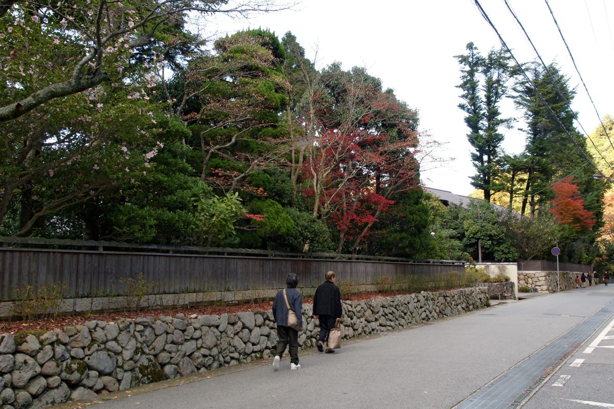 A quiet street with a stone wall and autumn trees in Arima Onsen