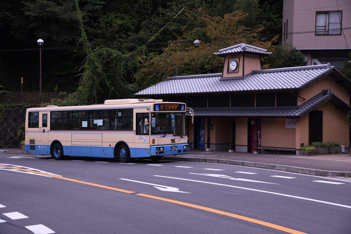 A Hankyu bus parked on a road beside a small building with a clock