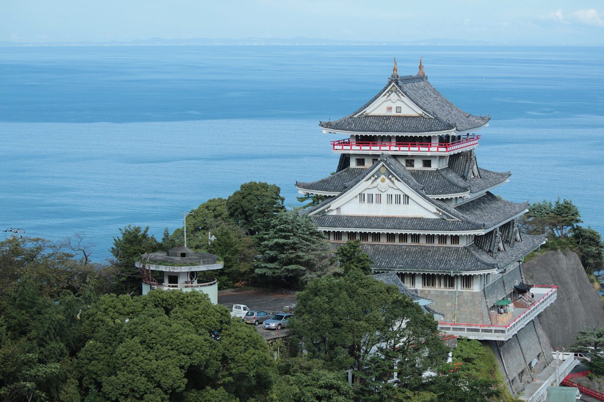 Atami Castle, a white castle-style building on a wooded hill above the sea
