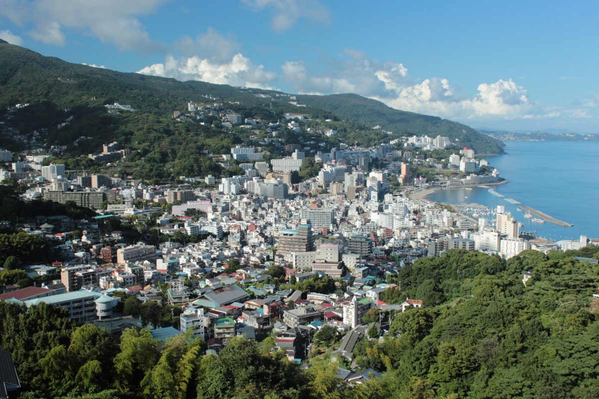 Hillside view over the town of Atami, with buildings spreading down to the bay and green hills behind