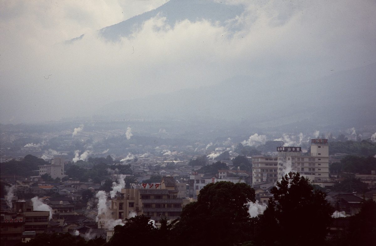 Columns of hot spring steam rising from rooftops across Beppu under a hazy sky