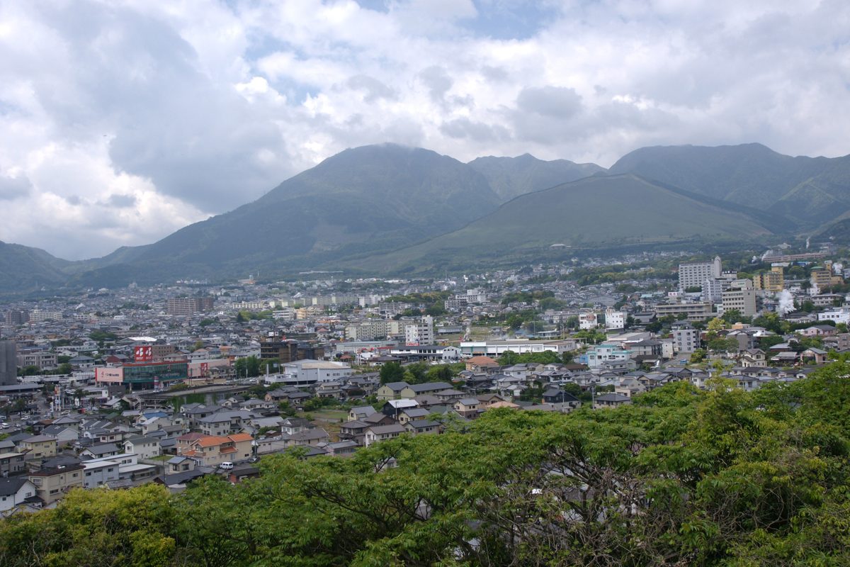 Daytime view over the rooftops of Beppu toward green mountains under a cloudy sky