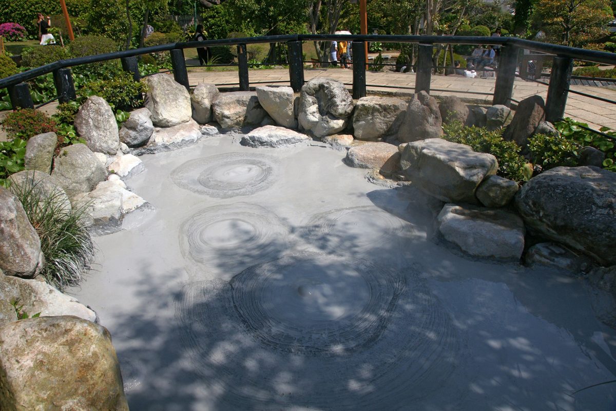 A pool of gray boiling mud ringed by rocks and a railing