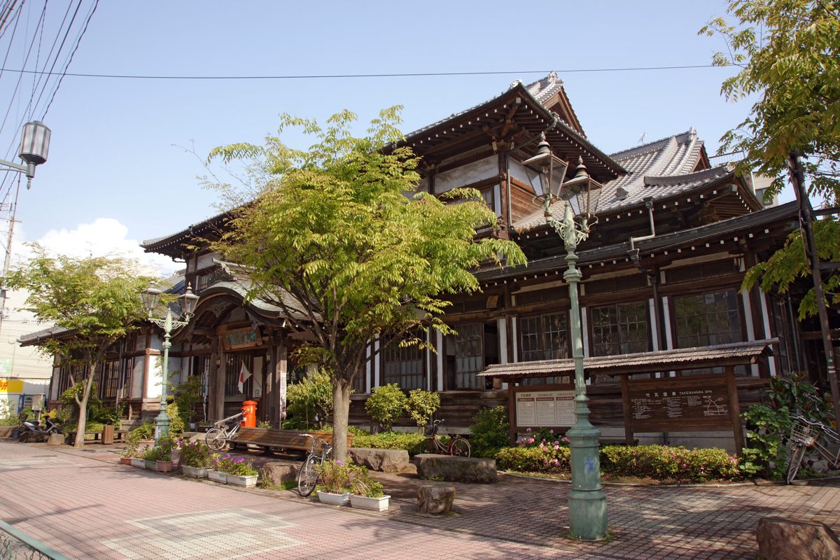 Wooden building of Takegawara Onsen with trees in front on a sunny day