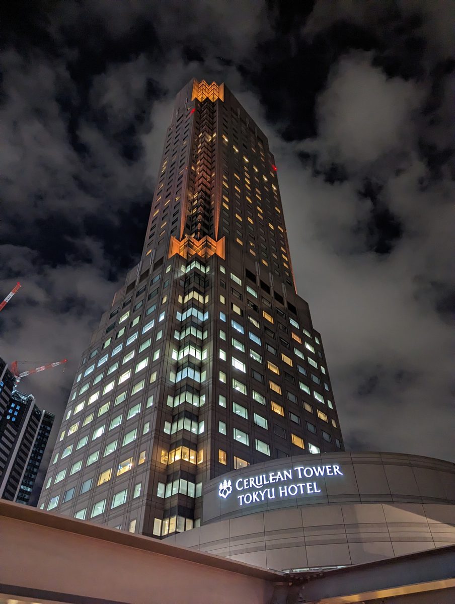 Cerulean Tower lit up at night, seen from below, with the hotel sign at its base