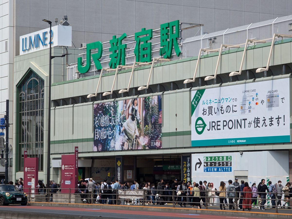 The JR Shinjuku Station building with large green station-name letters and crowds at the entrance