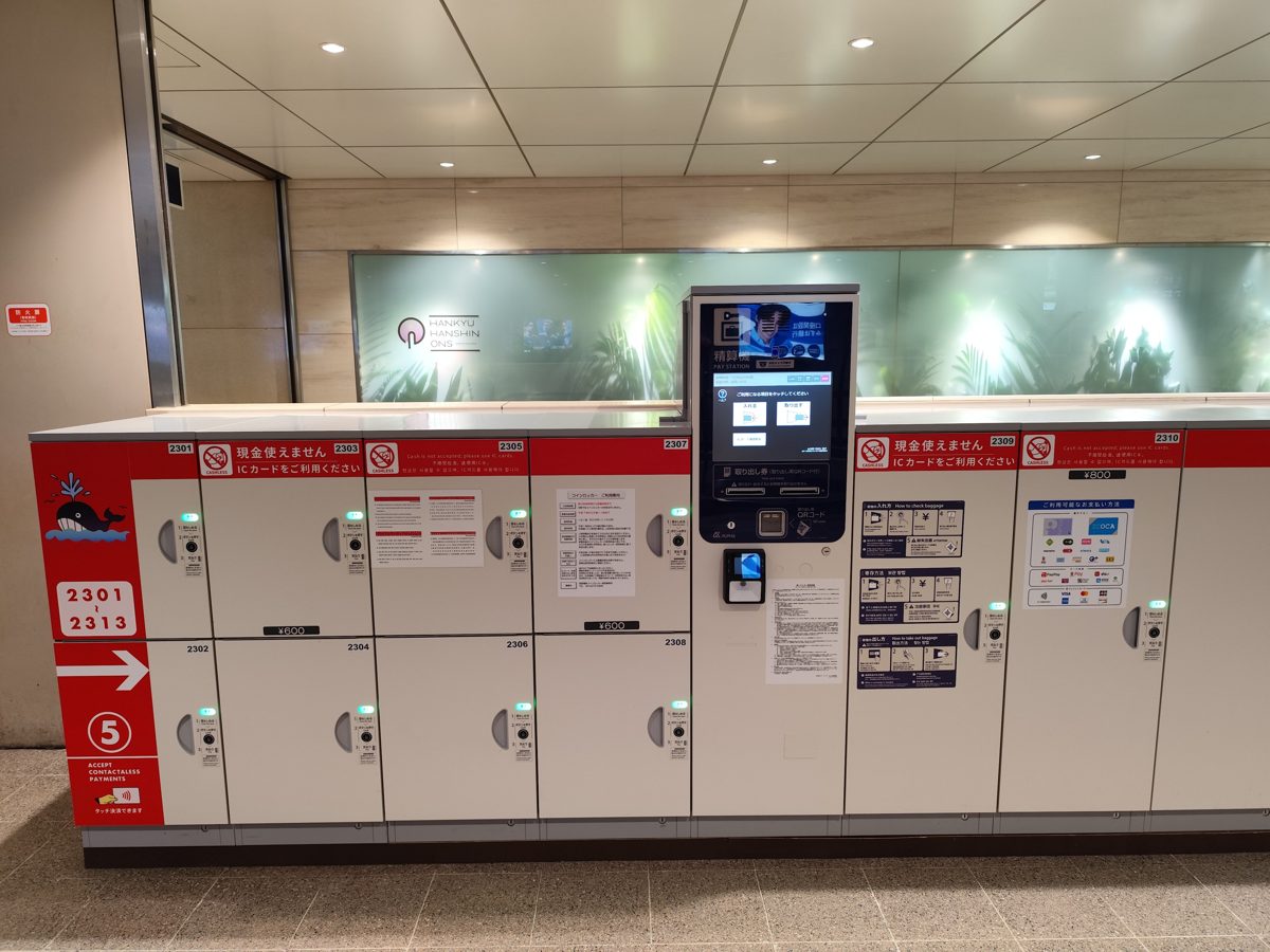 A row of white and red coin lockers with a touchscreen panel in a station passage