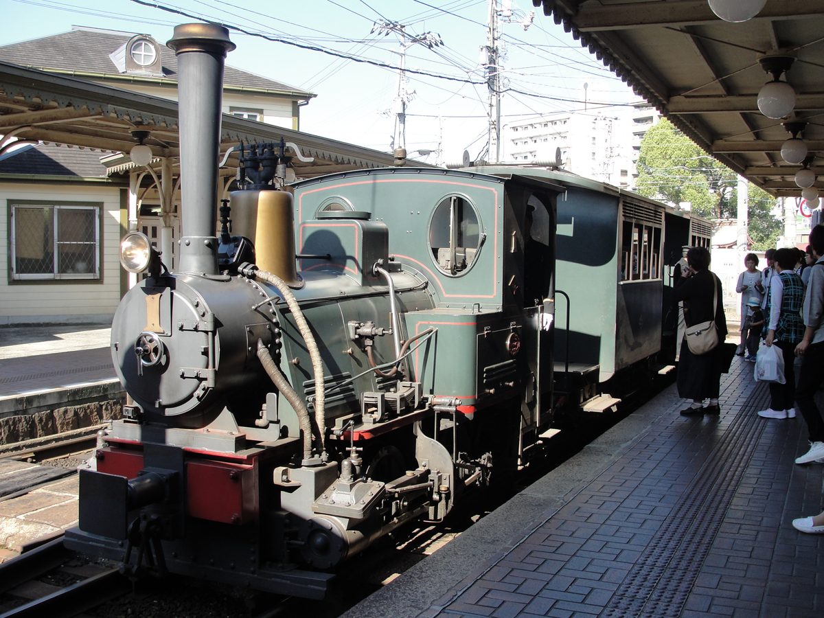 Green Botchan steam-style train waiting at the platform of Dogo Onsen Station