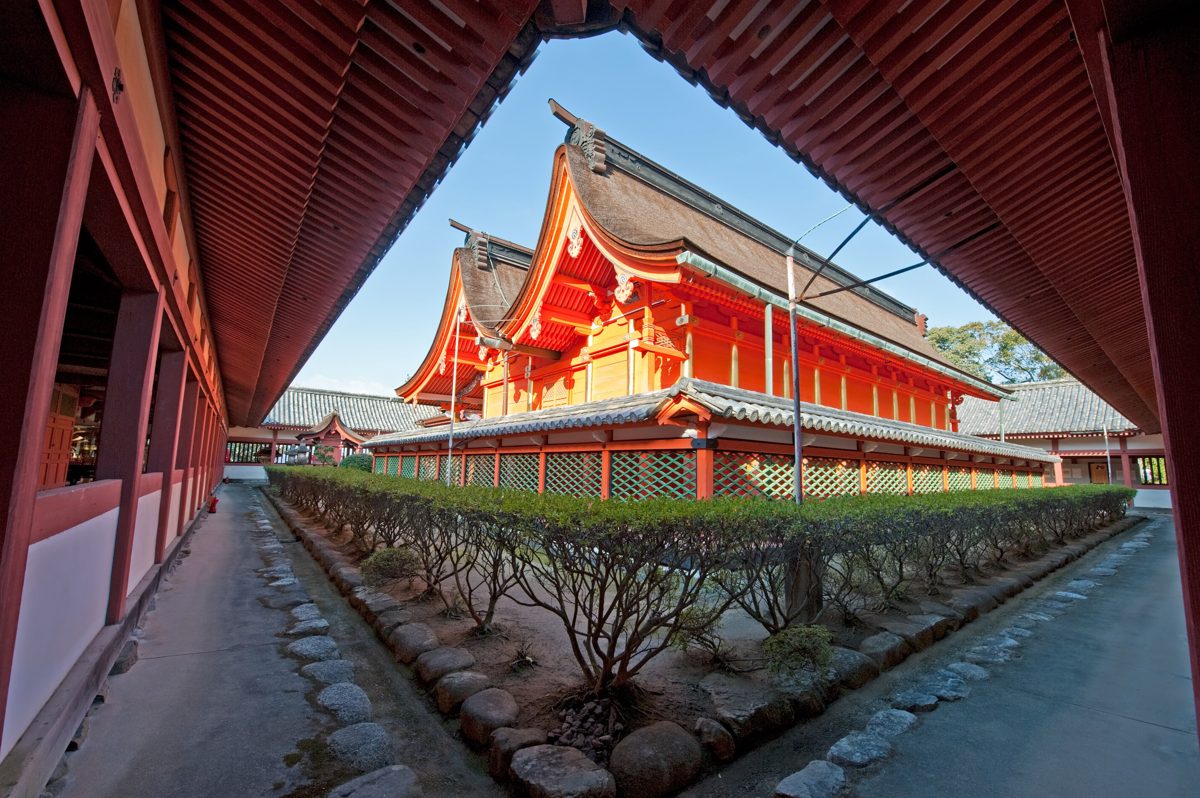 Vermilion main hall of Isaniwa Shrine seen through a covered corridor under a blue sky