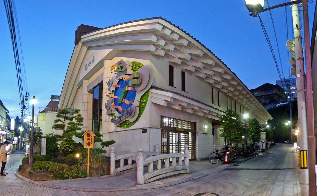 A white public bathhouse with a decorated gable and a small arched railing, on a quiet street at dusk