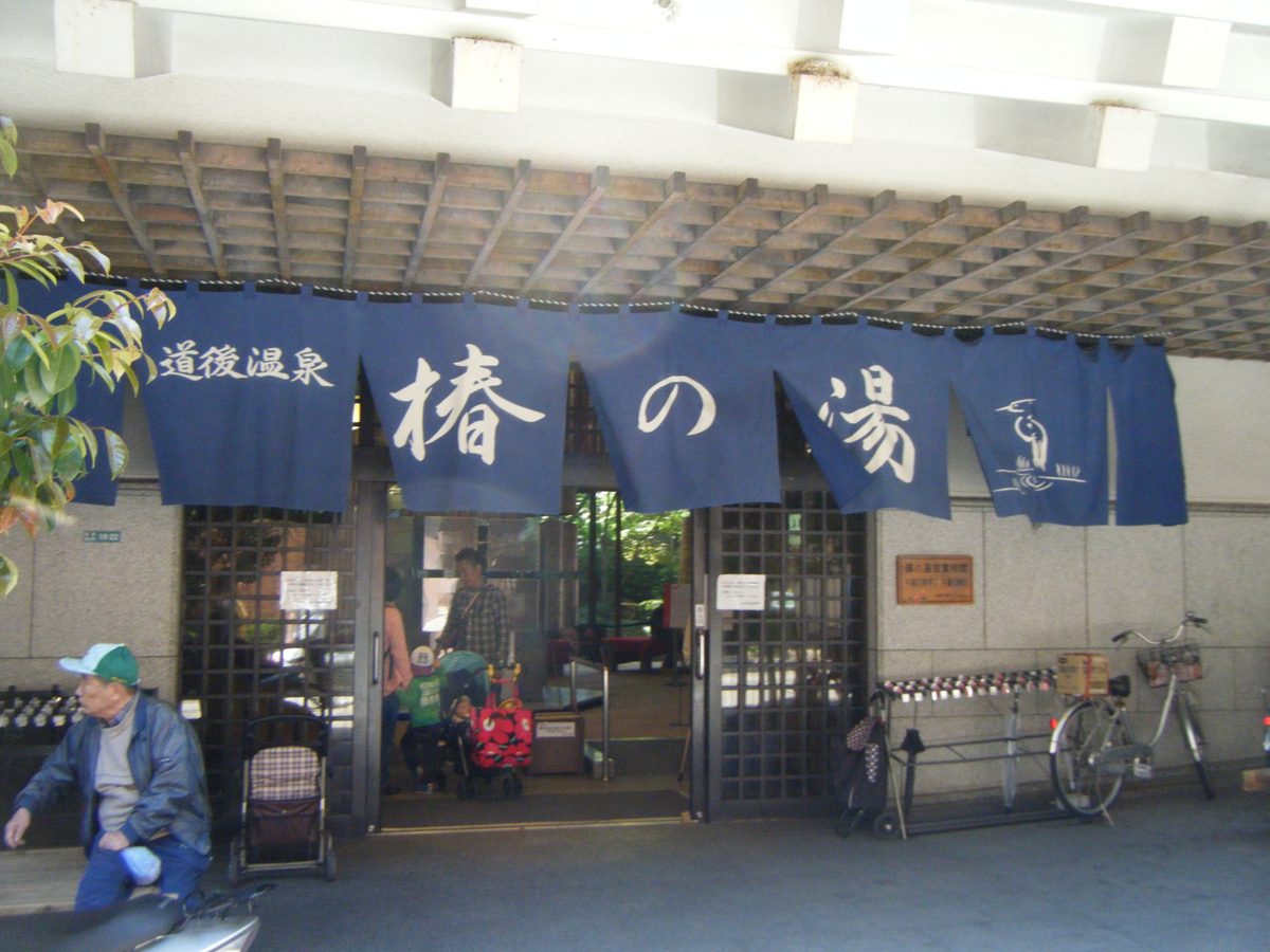 The entrance of a public bathhouse in Dogo with navy curtains reading Tsubaki-no-Yu