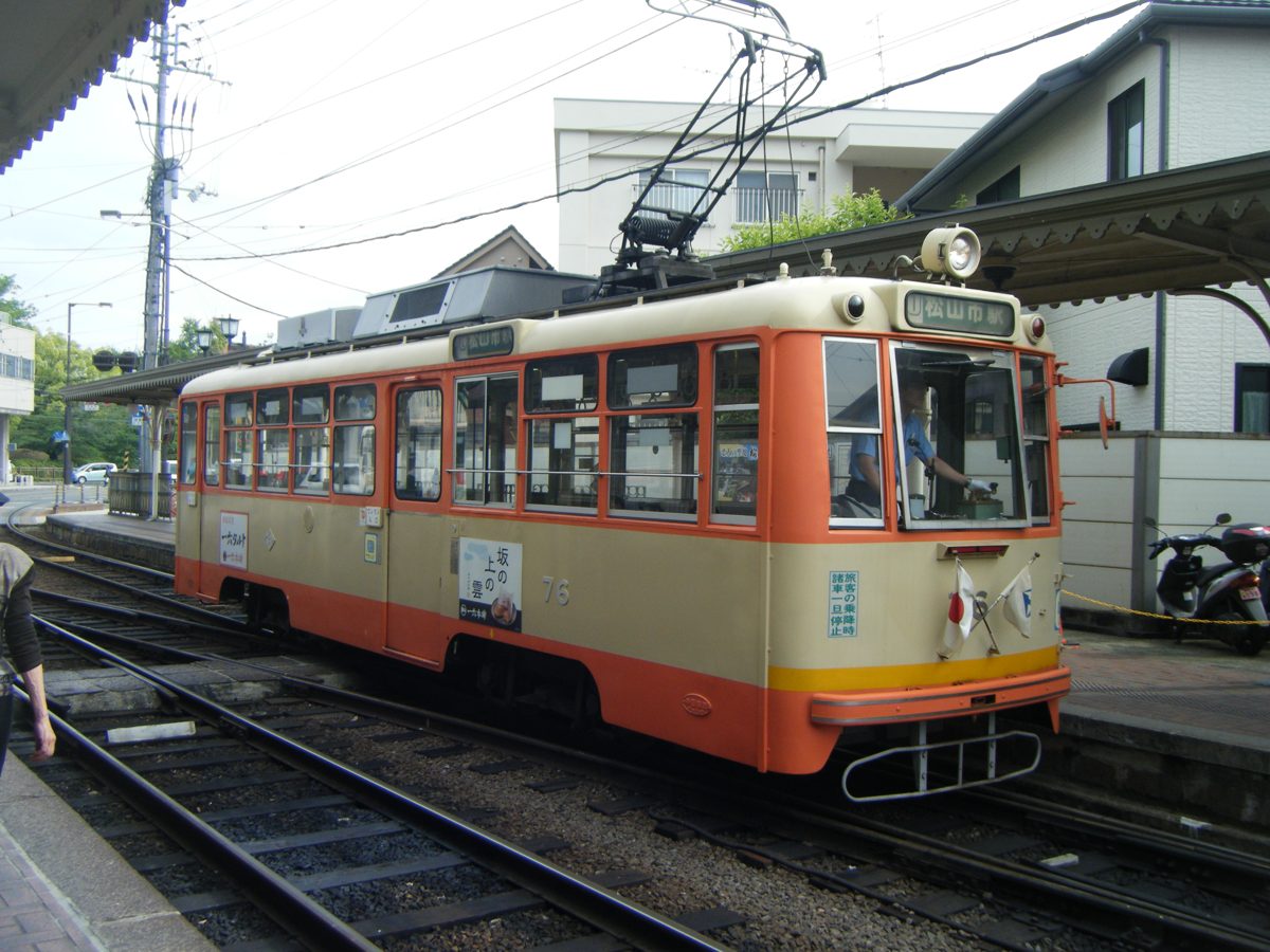An orange and cream Iyotetsu streetcar at a tram stop