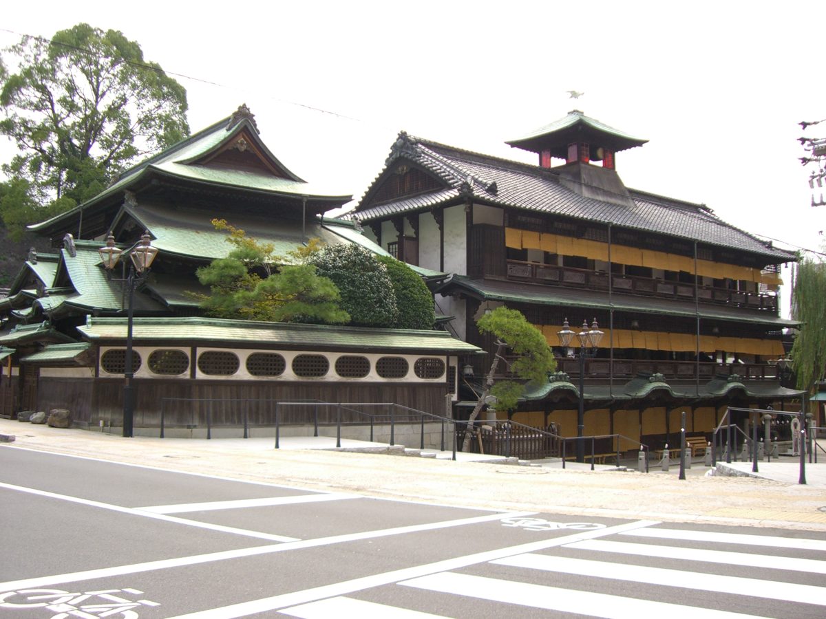 The wooden multi-story Dogo Onsen Honkan bathhouse under a blue sky