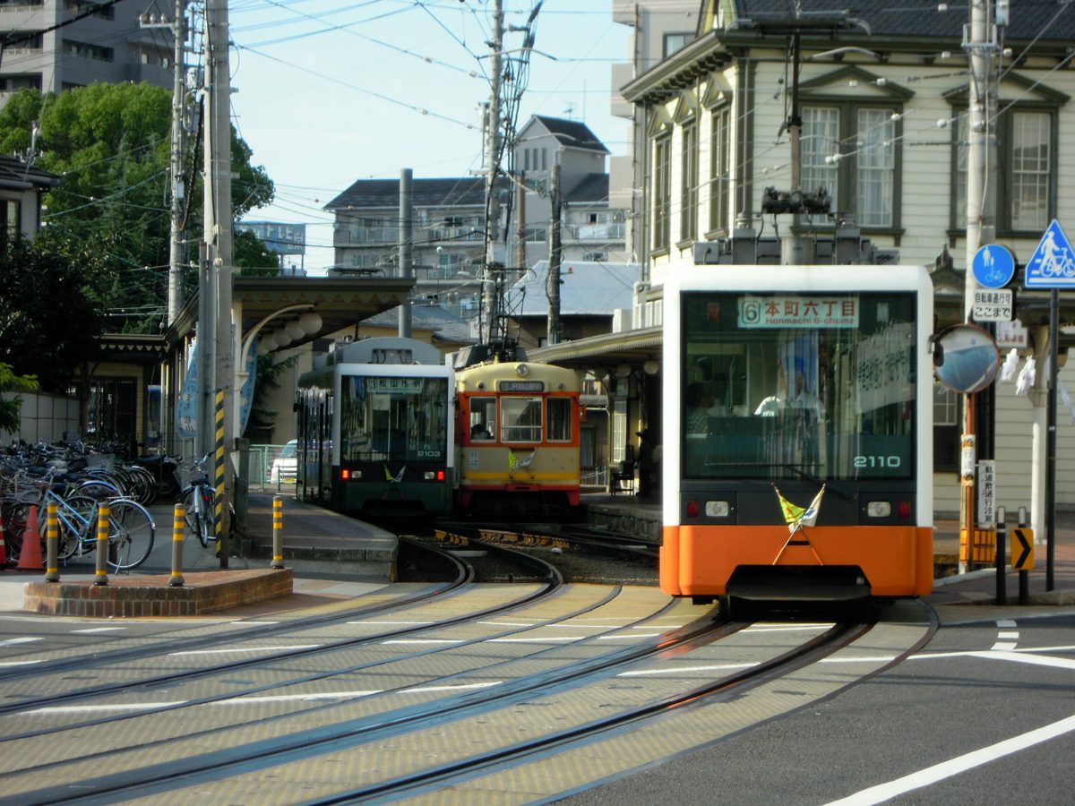 Orange Iyotetsu trams waiting at Dogo Onsen Station next to an old-style station building