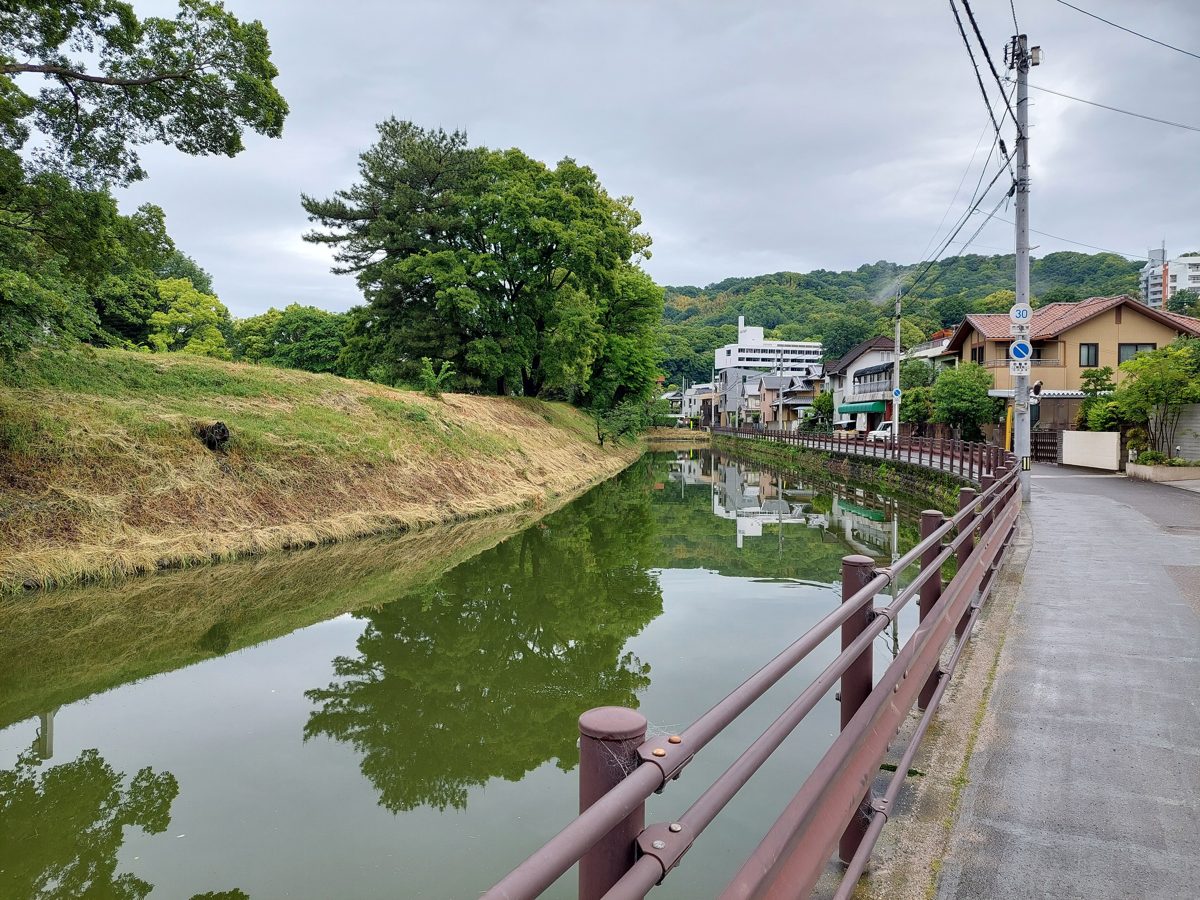 A moat lined with trees and a railing at Dogo Park in Matsuyama on a cloudy day