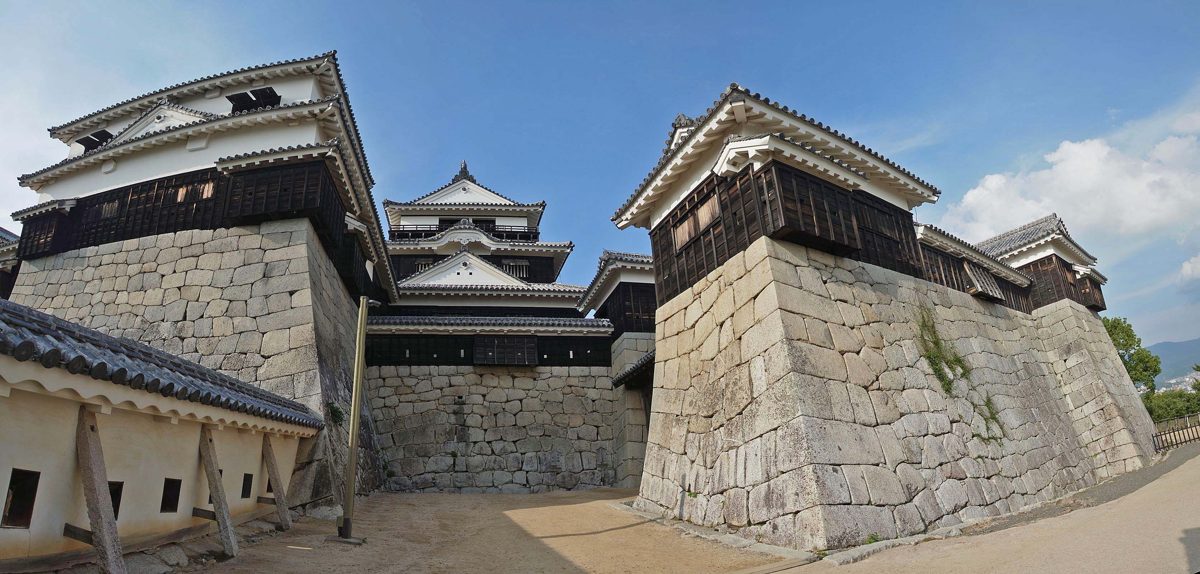 Stone walls and white-walled towers of Matsuyama Castle under a blue sky